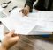 Hands exchanging financial documents, symbolizing the need for stricter disclosure of industry payments to doctors in medical education.