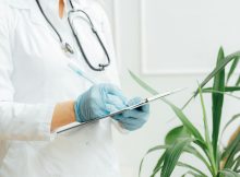Doctor in white coat with stethoscope writing on a clipboard, representing NMC’s initiative to provide all doctors in India with unique identification numbers.