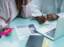Researchers and students collaborating with journals and laptops, highlighting the need for nationwide access to scholarly research under One Nation, One Subscription.