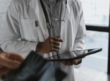 Doctor in white coat holding a tablet, symbolizing the need for affordable medical education and accessible healthcare in India.